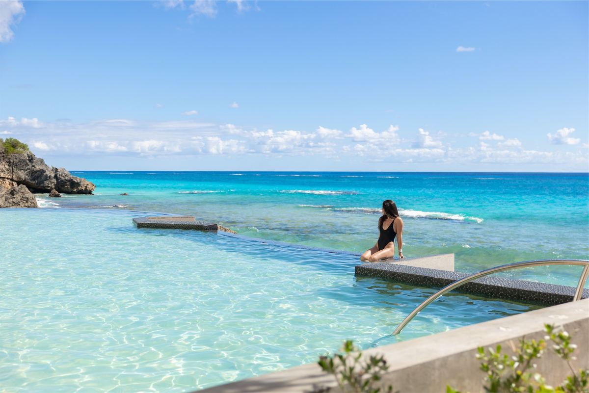 Guest resting at the edge of an infinity pool that reads into the reef beyond