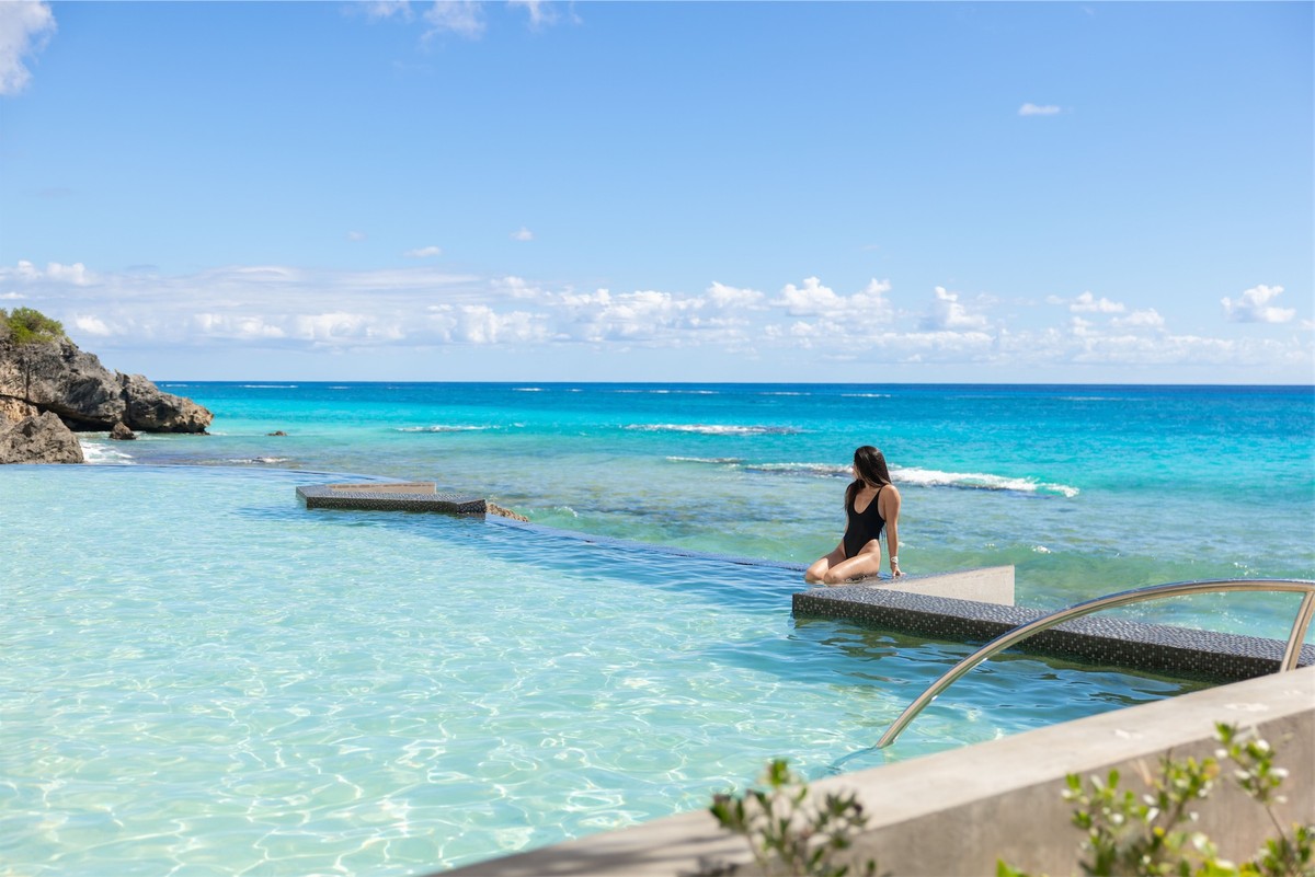 Guest resting at the edge of an infinity pool that reads into the reef beyond