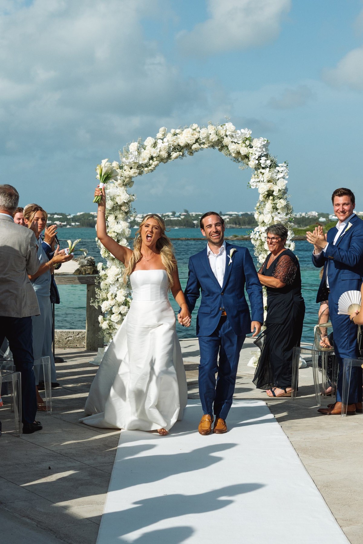 Paige raises her bouquet as she and Cam walk back up the aisle on Hawkins Island, Bermuda