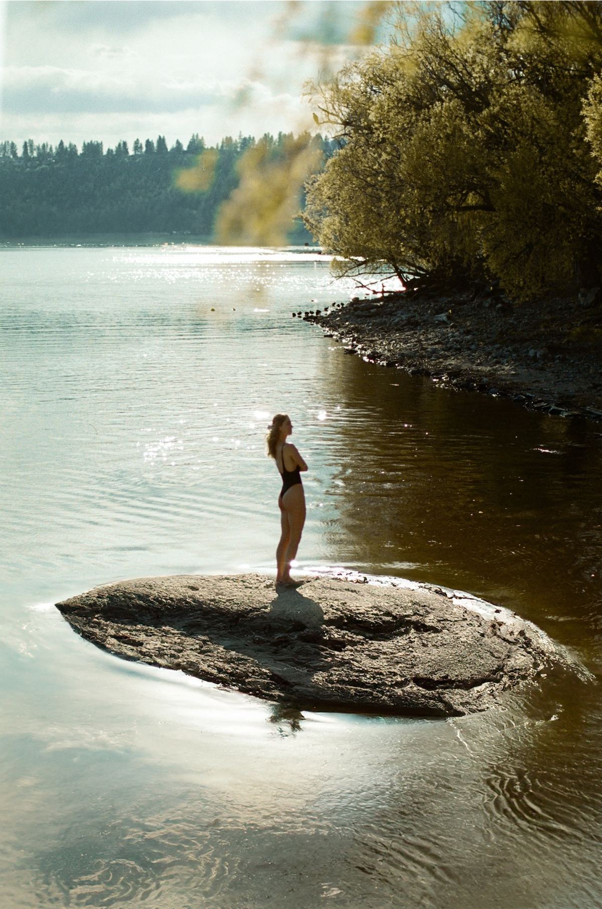 Model standing on a small rock island in the middle of a calm wooded lake
