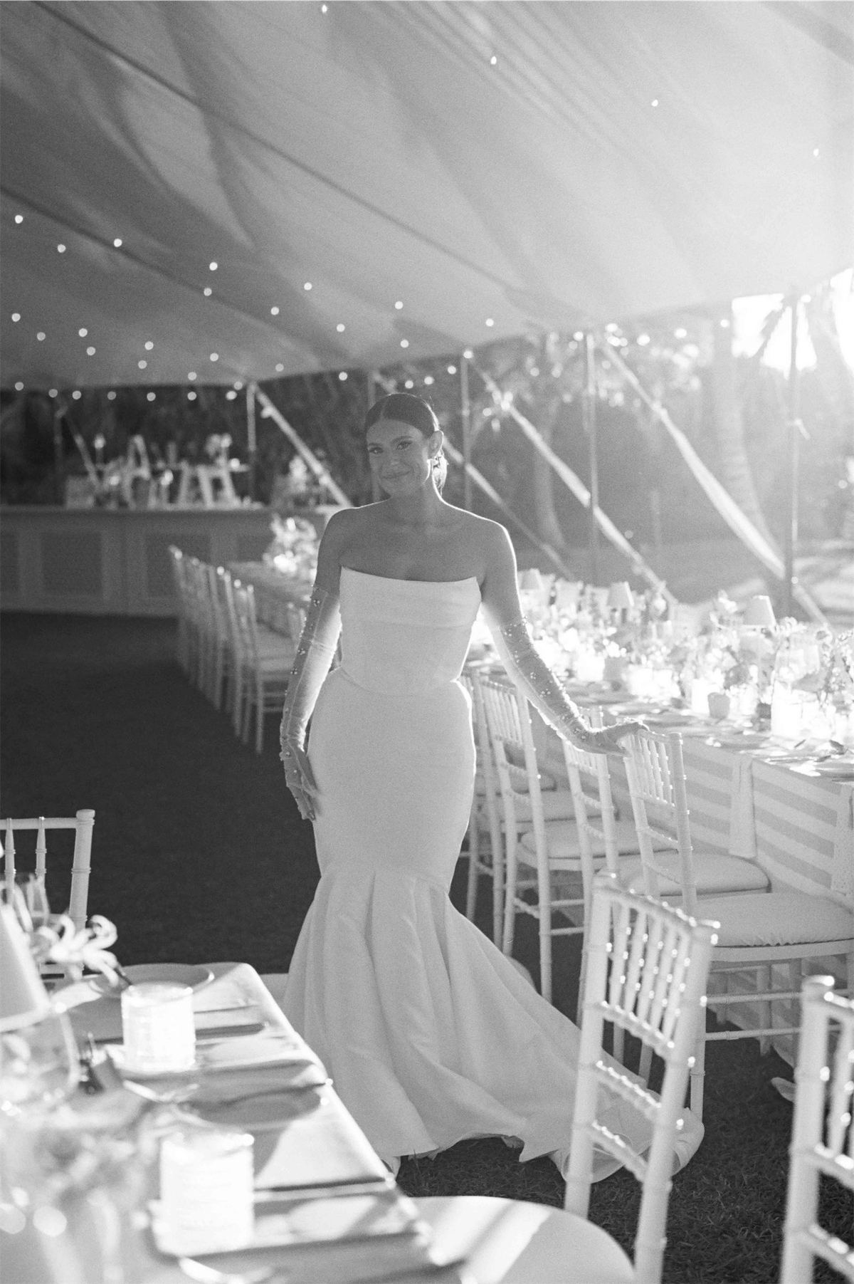 Black and white view of the bride walking through the tented reception past set tables