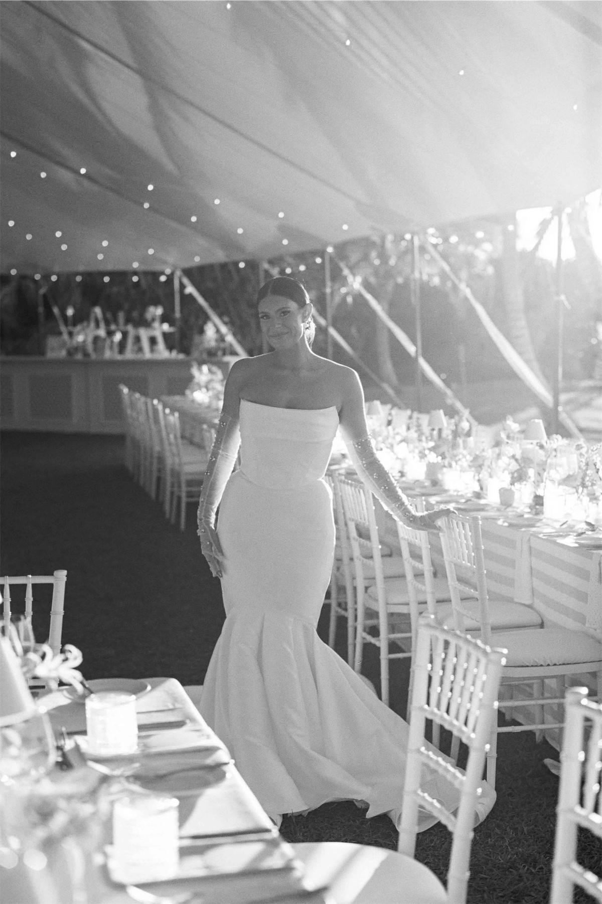 Black and white view of the bride walking through the tented reception past set tables