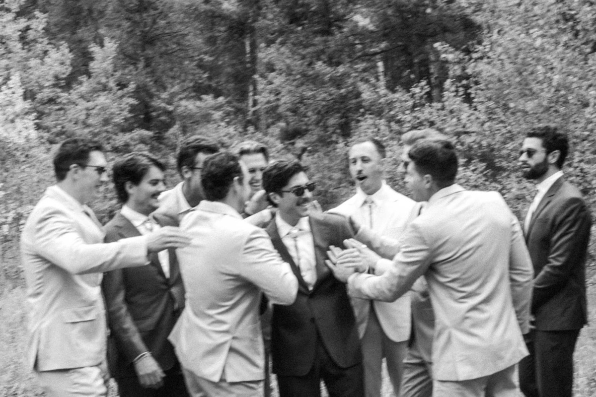 Owen's groomsmen crowd around him cheering at a mountain ranch among the aspens, black and white