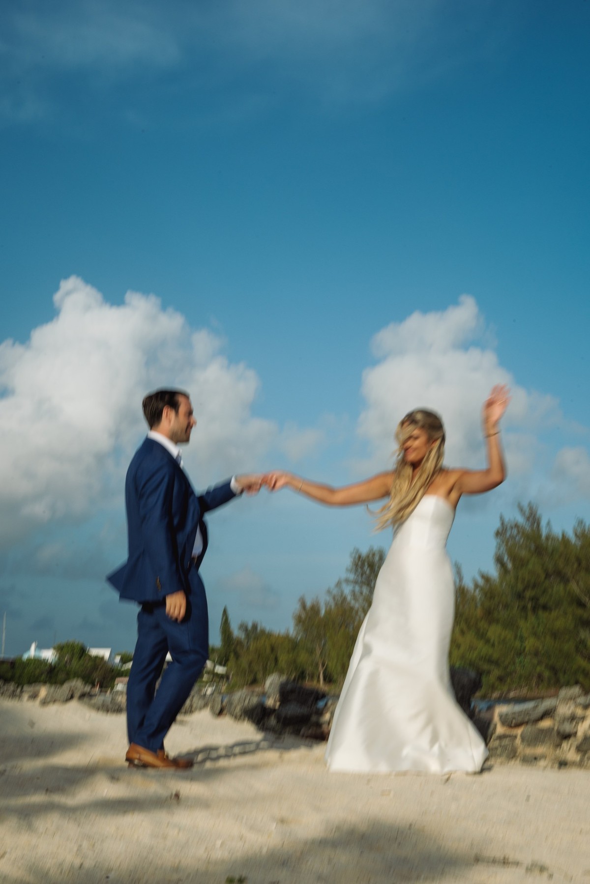 Cam twirls Paige on the beach under bright summer clouds on Hawkins Island, Bermuda