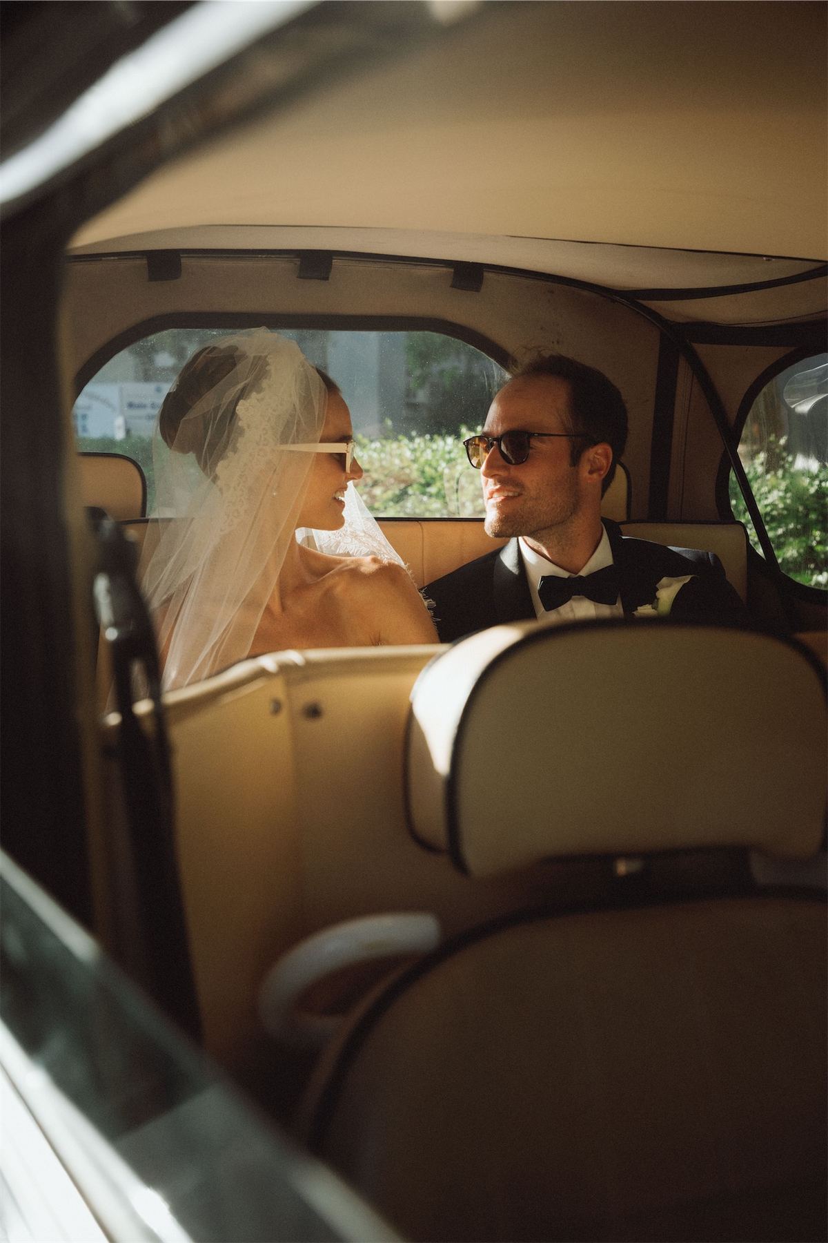 Bride and groom riding in the back of a vintage car, veil against the window