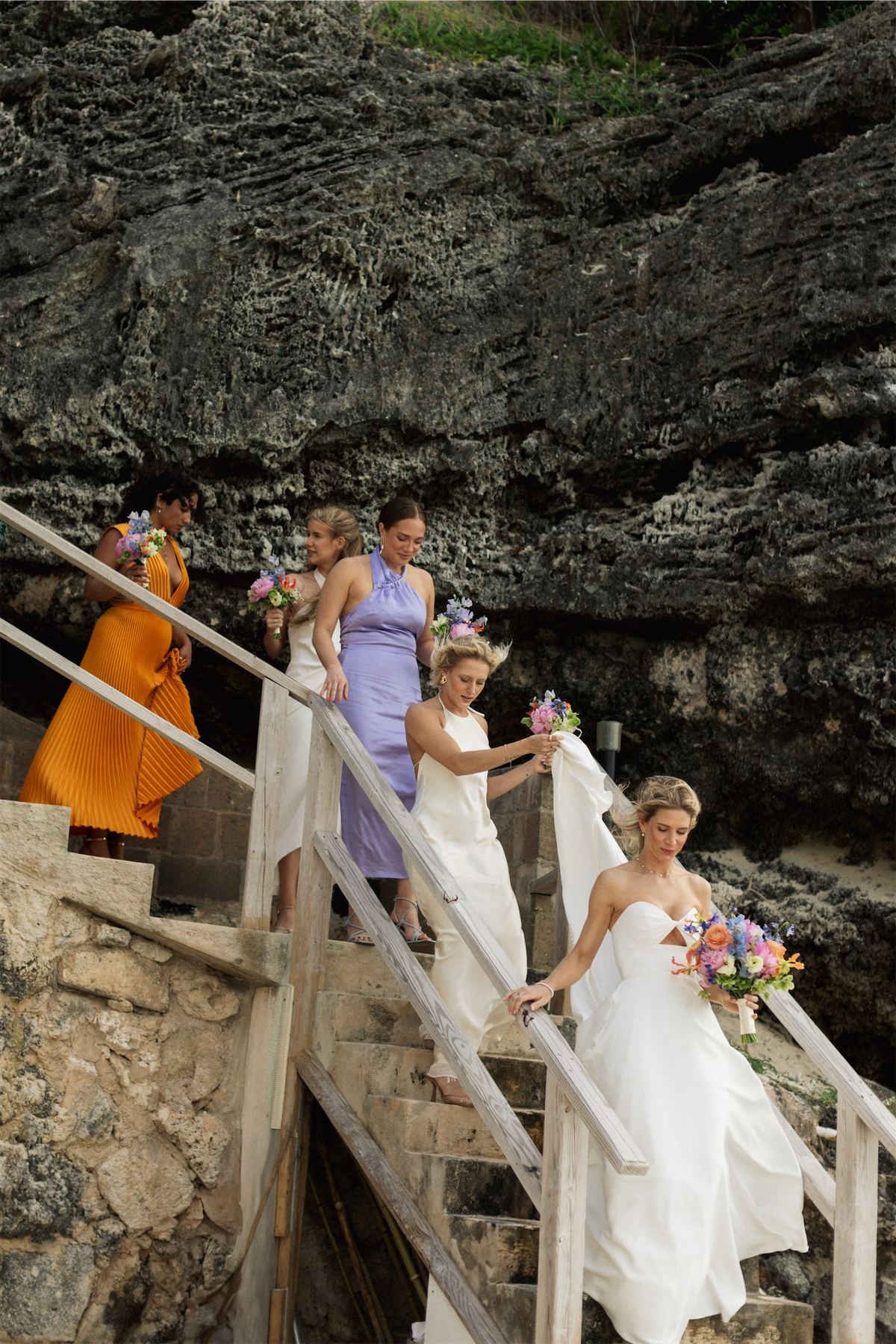 Bride and her bridesmaids descending a wooden staircase built into the cliff