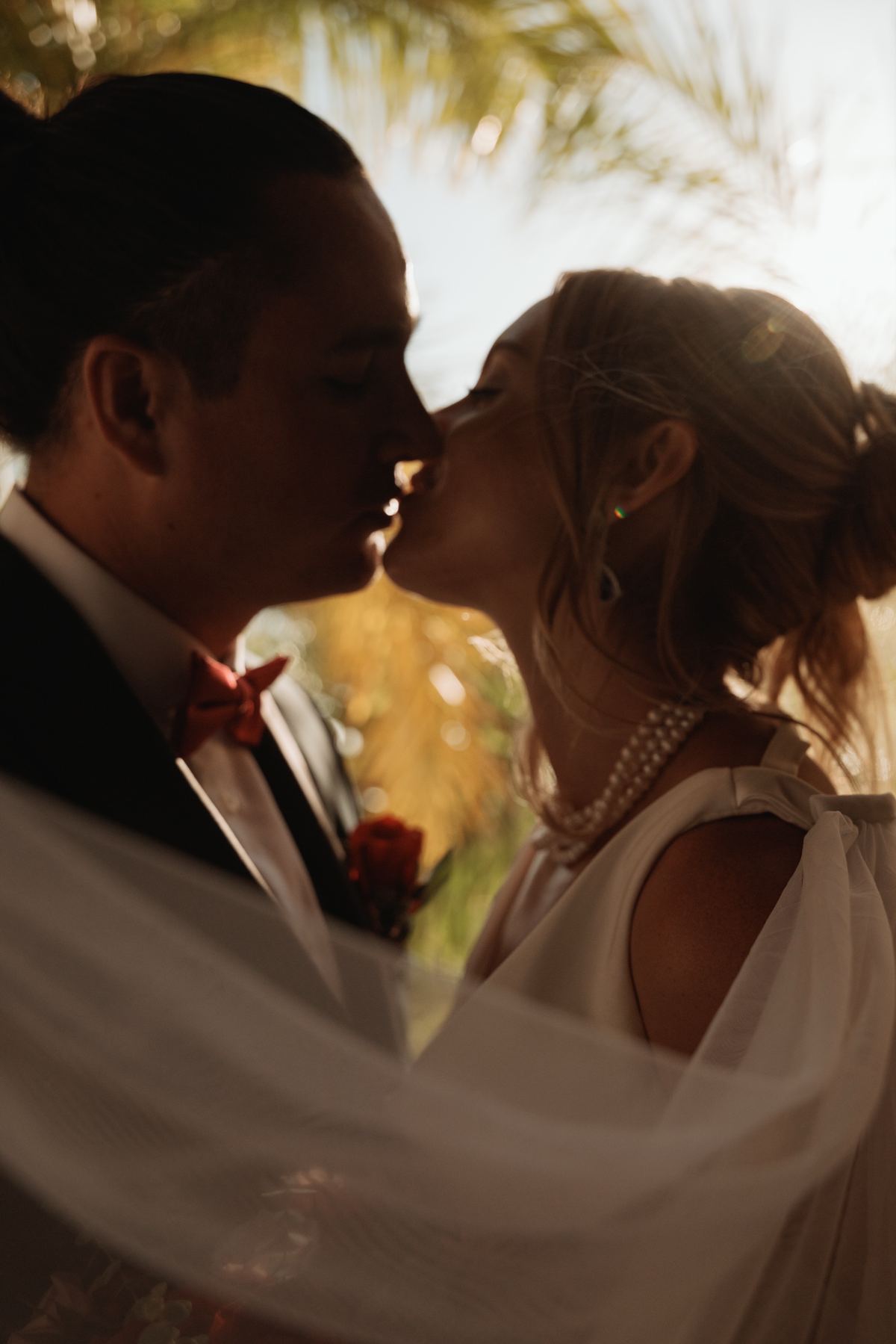 Bride and groom kissing under flowing veil at sunset destination wedding