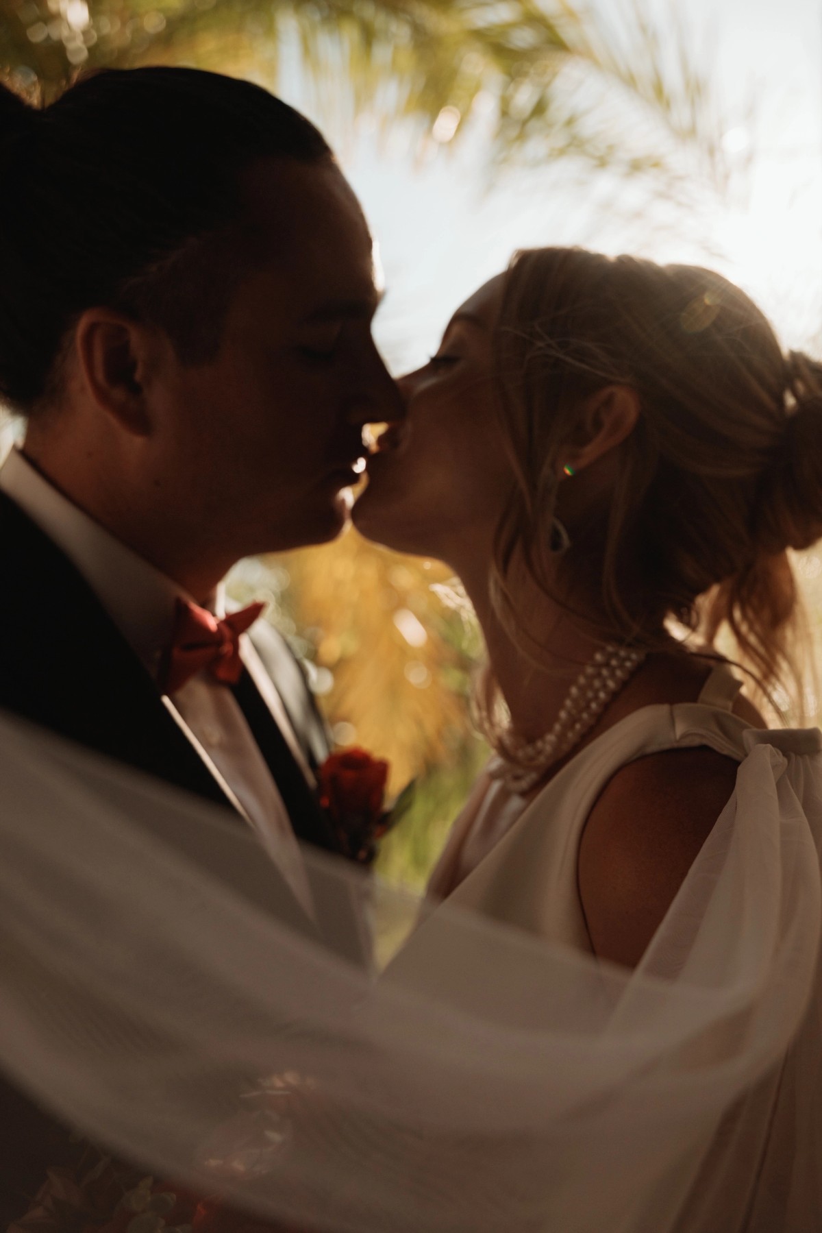 Bride and groom kissing under flowing veil at sunset destination wedding