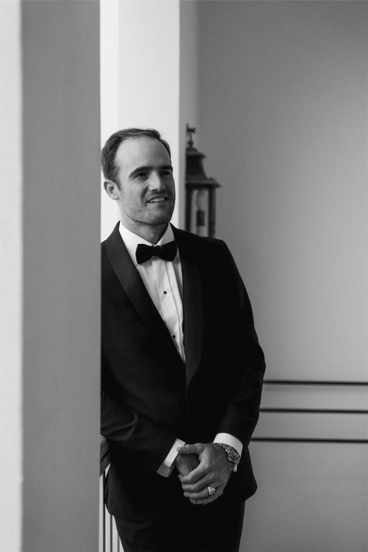 Black and white portrait of the groom in a tuxedo against a white column