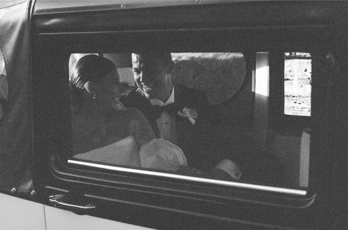 Black and white of the couple kissing in the car, seen through the window