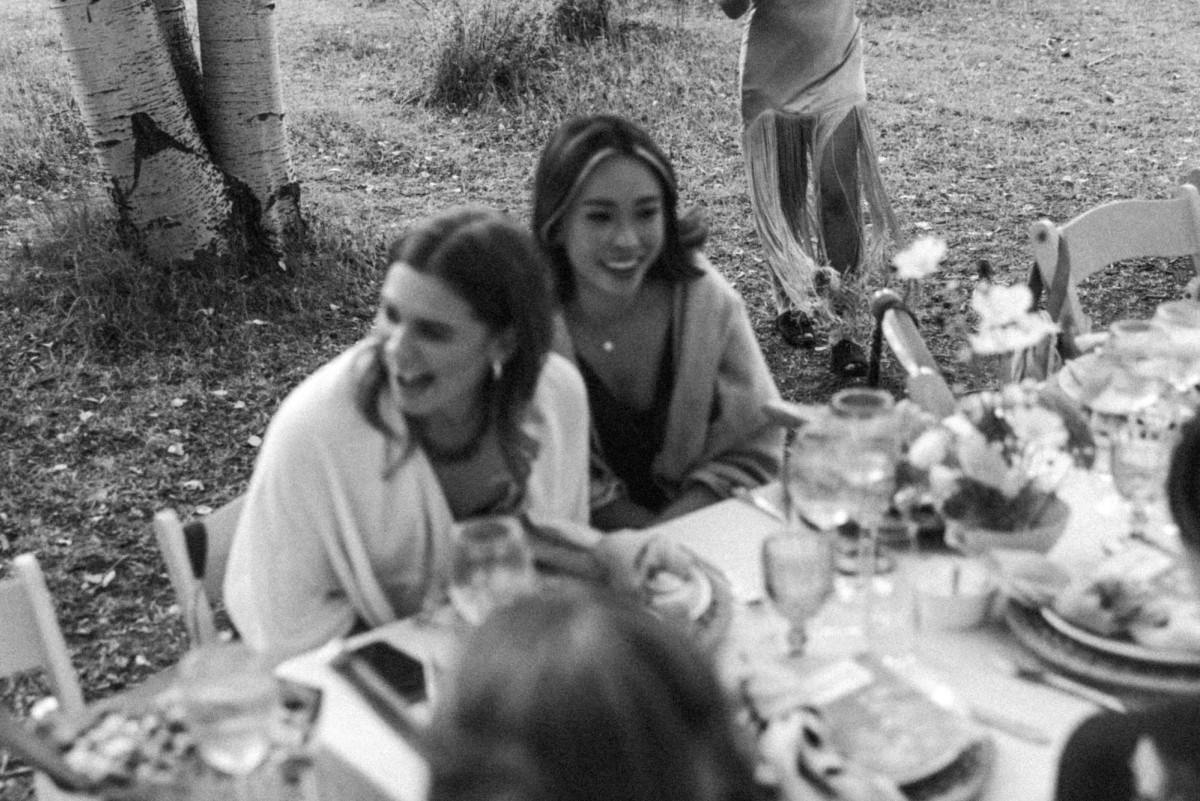 Two guests laugh at the reception table at a mountain ranch among the aspens, black and white