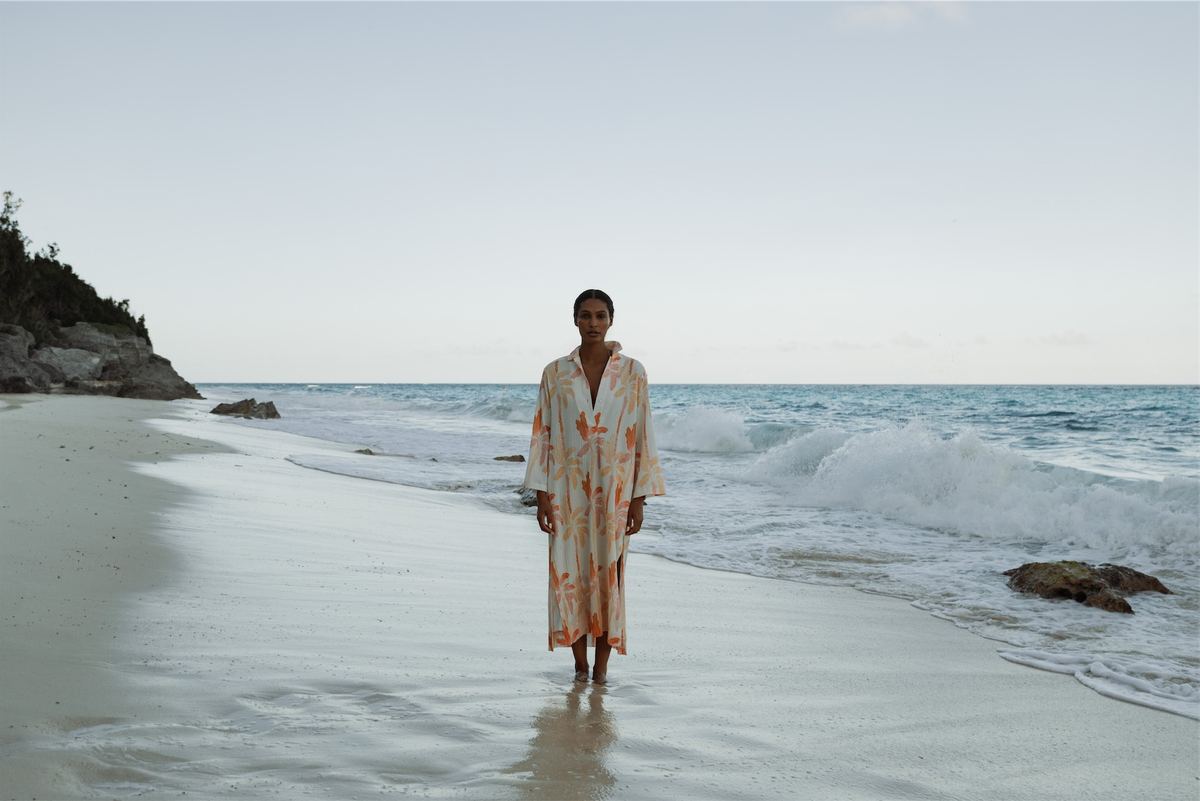 Model in a printed kaftan standing ankle deep in the surf on an empty beach