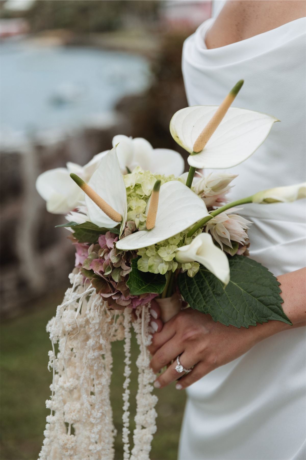 Detail of the bride holding a white anthurium bouquet with trailing ribbons