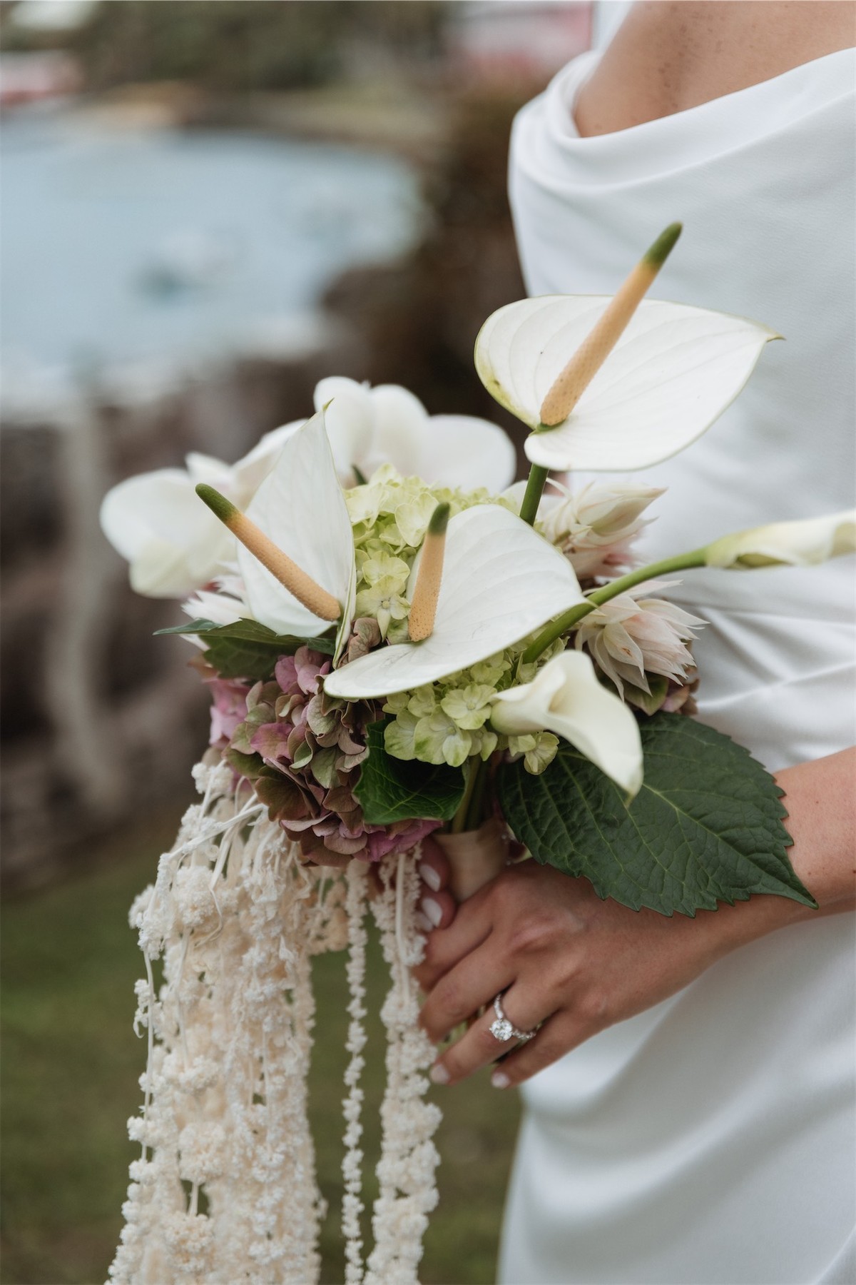 Detail of the bride holding a white anthurium bouquet with trailing ribbons