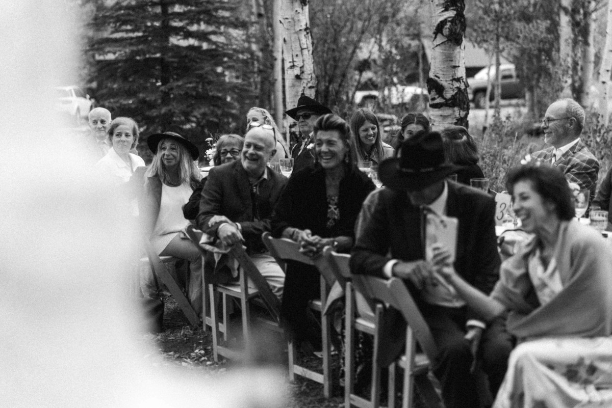 Guests in cowboy hats laugh during the toasts at a mountain ranch among the aspens, black and white