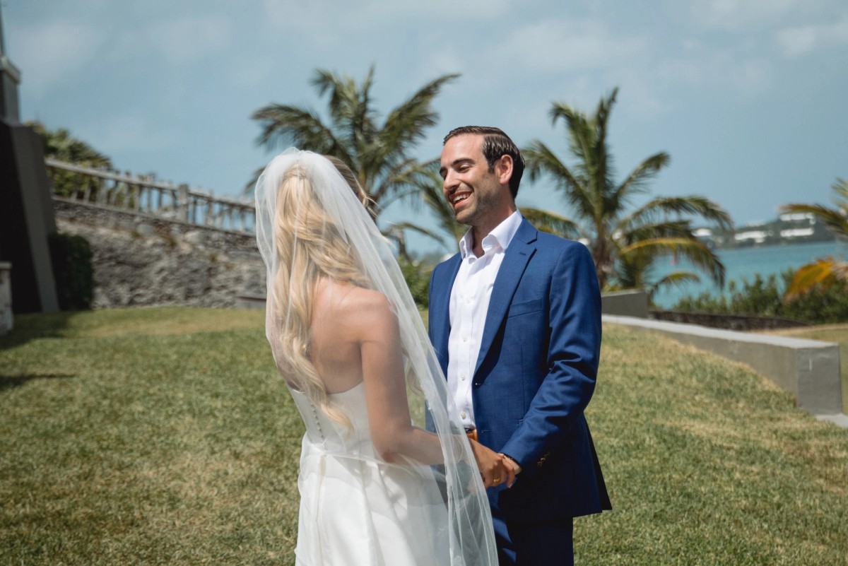 Cam grins at Paige on the lawn with palm trees and the bay behind them on Hawkins Island, Bermuda