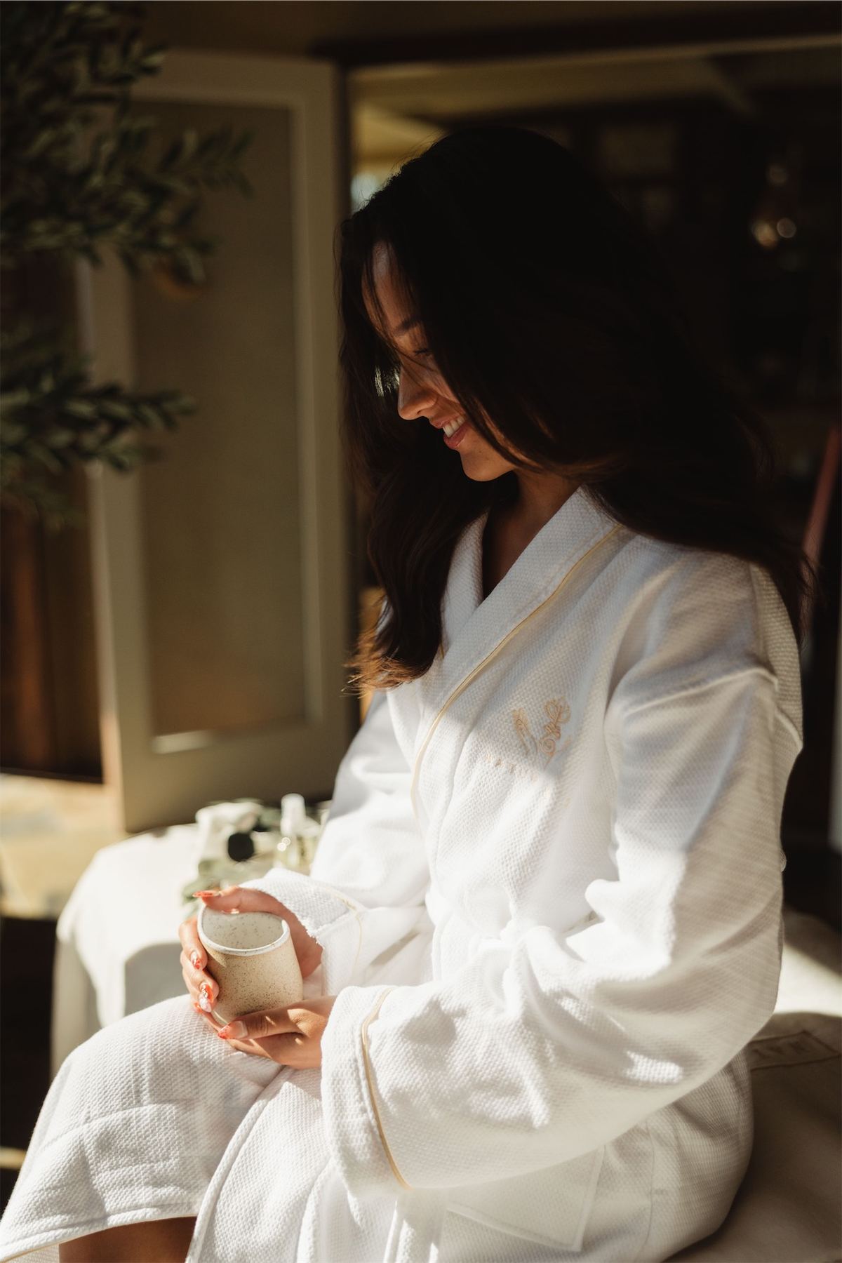 Woman in a white spa robe holding a candle in soft window light