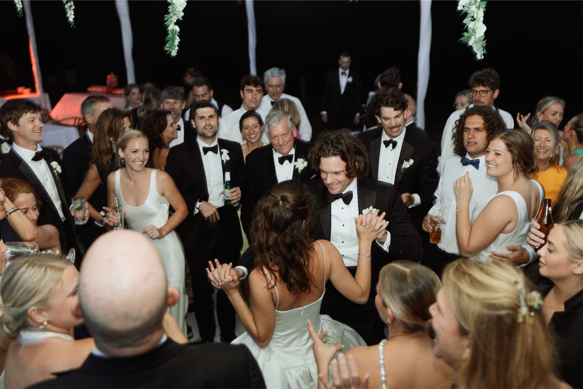 Black tie guests crowding the dance floor beneath hanging white florals