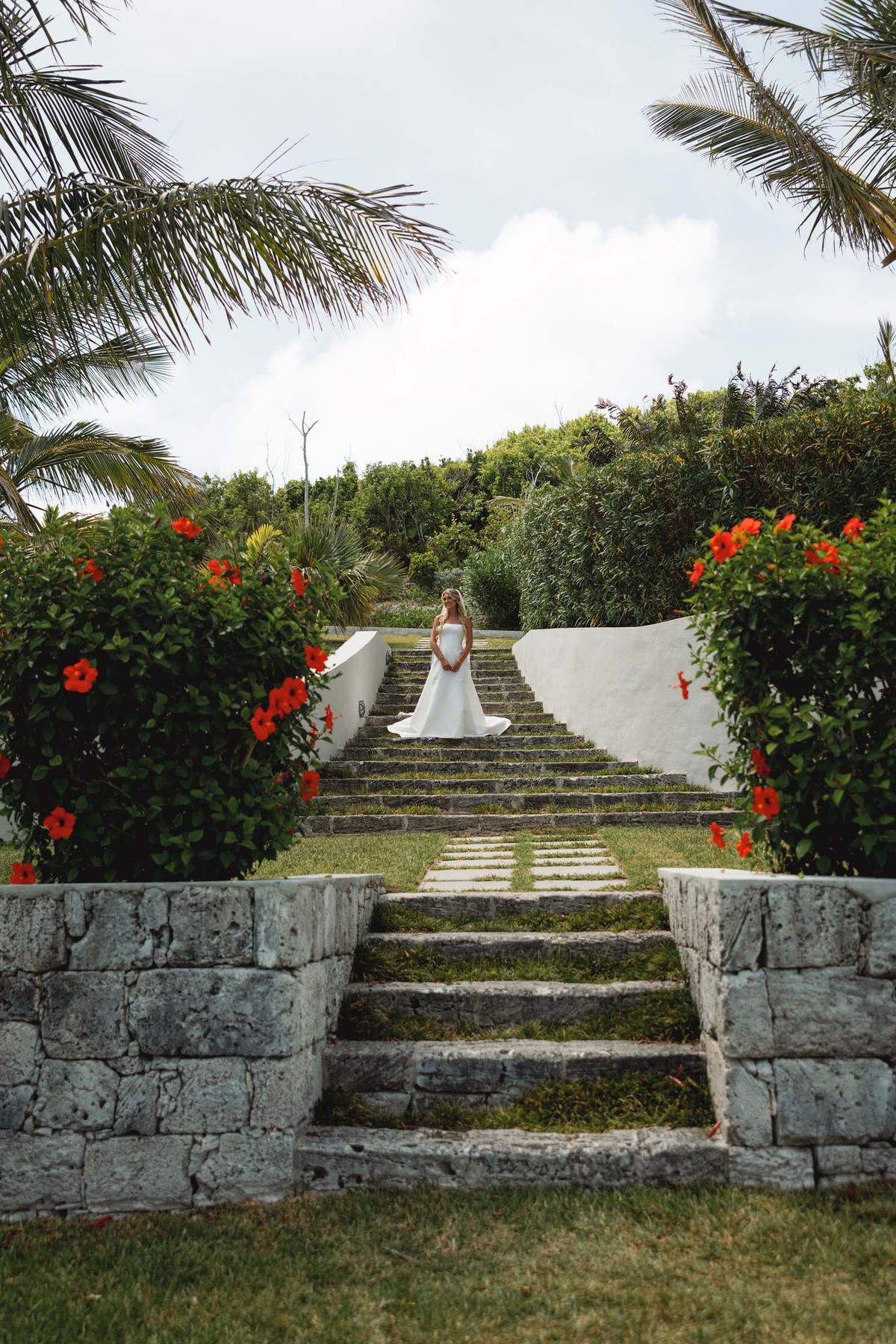 Paige descends the garden steps between red hibiscus to the first look on Hawkins Island, Bermuda