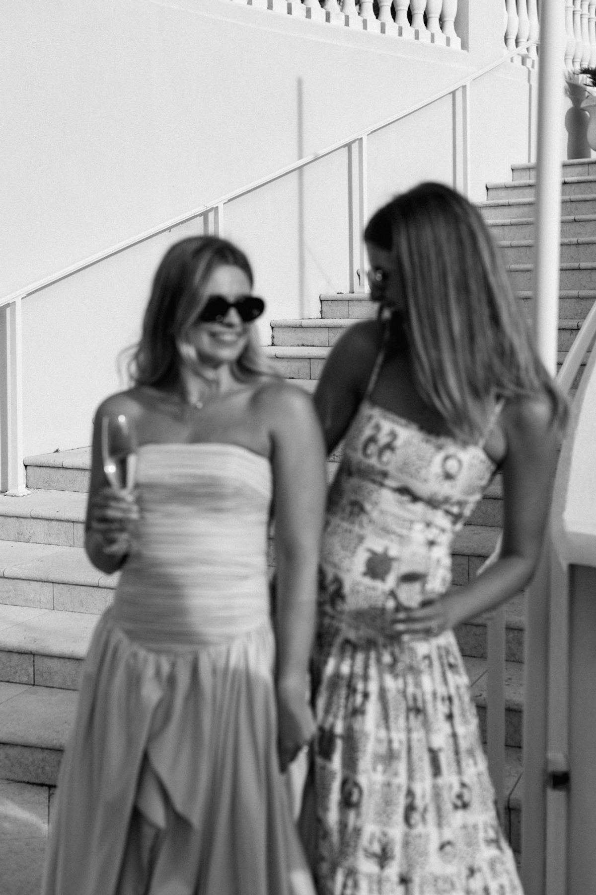 Black and white of two guests talking over drinks on a white staircase