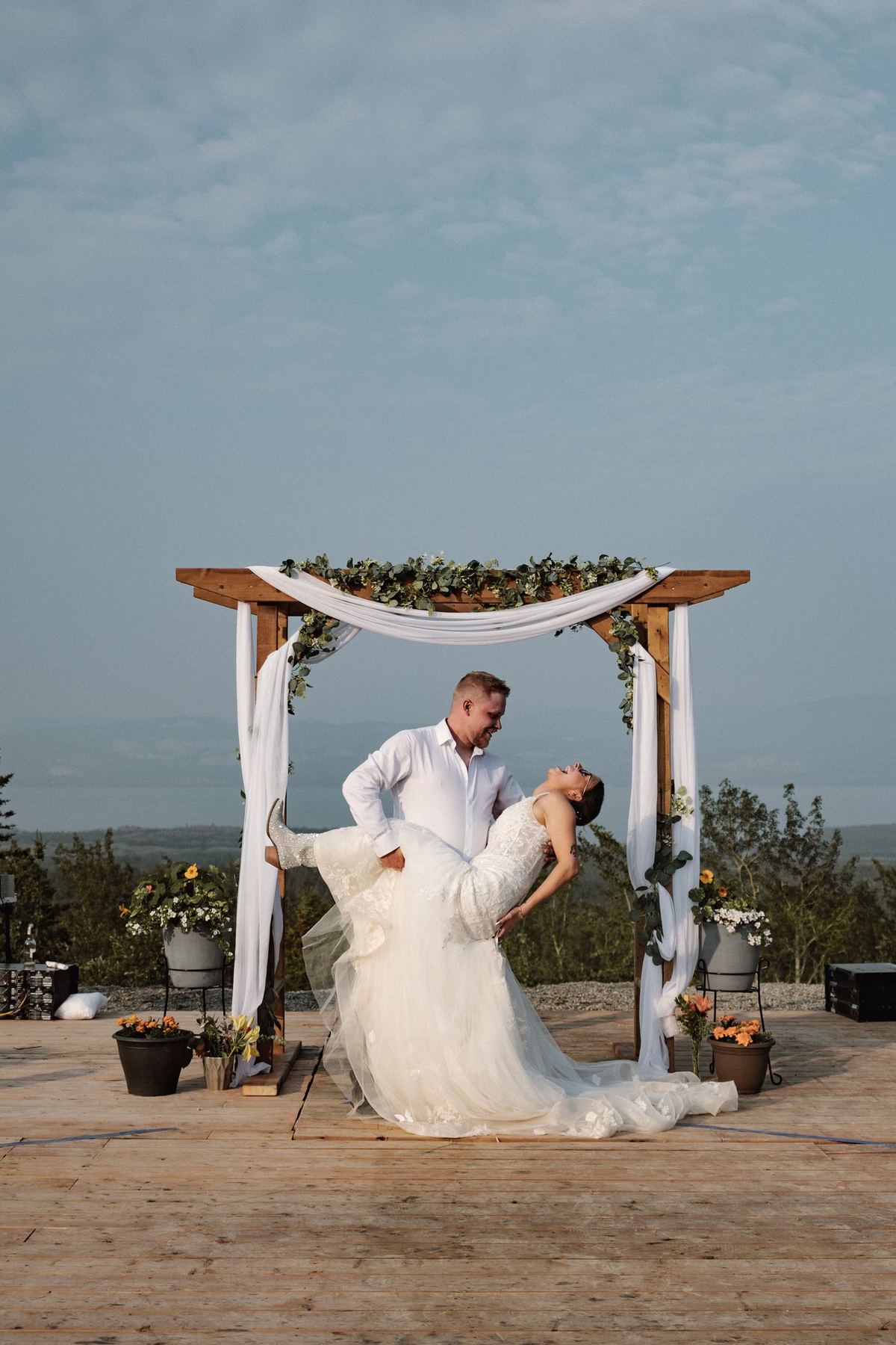 Bride and groom dip kiss beneath the ceremony arch on a mountaintop deck
