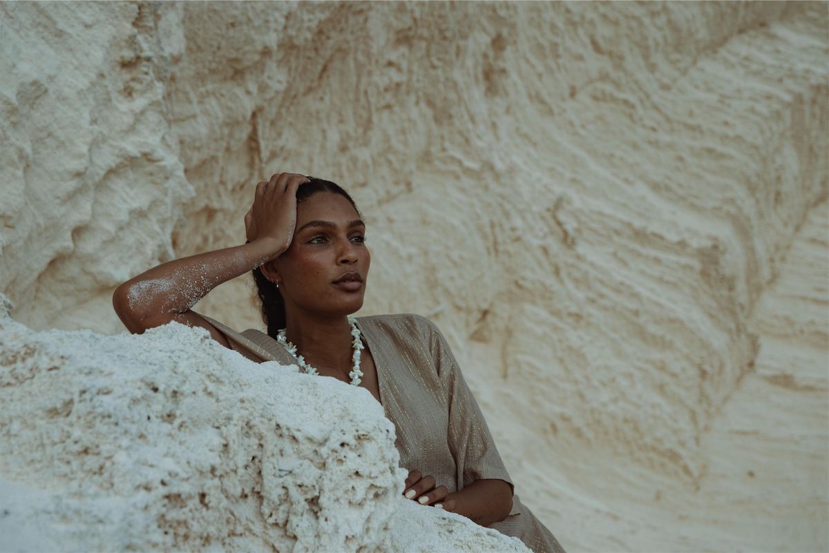Model in a linen shirt leaning back against a pale limestone cliff