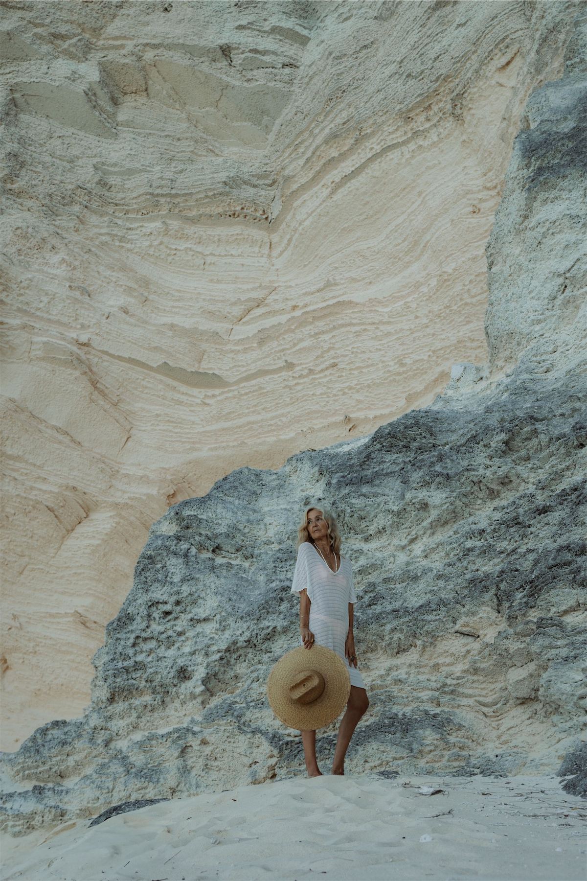 Distant figure in a white dress and straw hat perched on pale eroded rocks