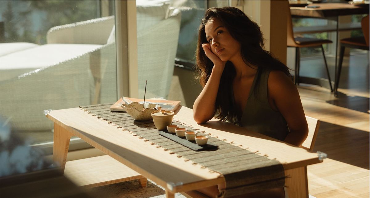 Woman resting her chin on her hand at a low table set with tea and incense