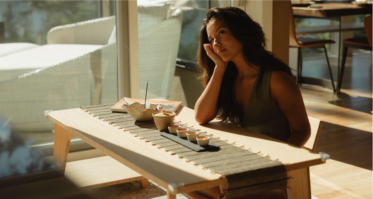 Woman resting her chin on her hand at a low table set with tea and incense