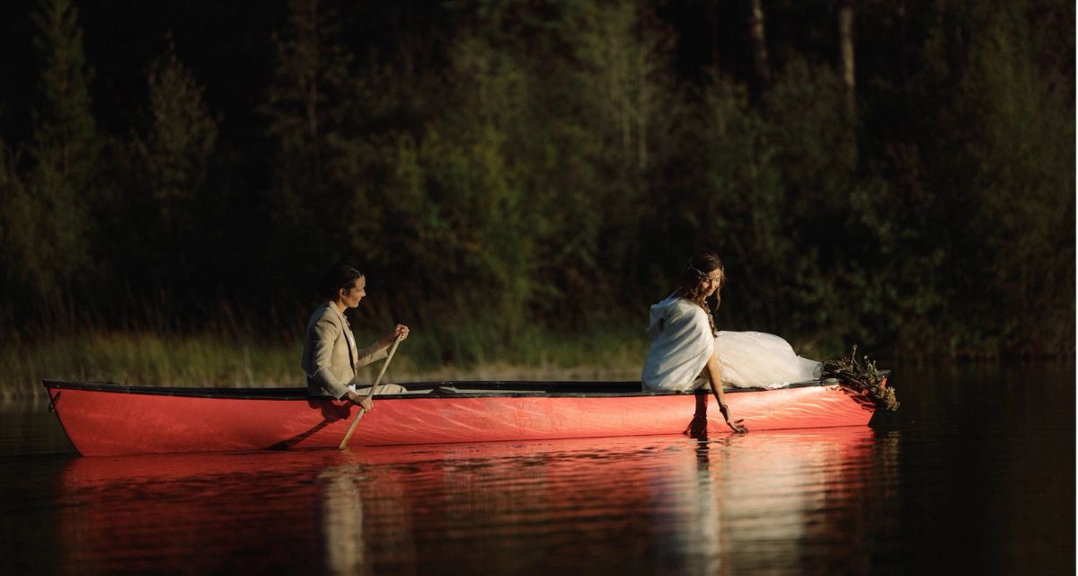 Couple paddling a red canoe across a mirror-still forest lake