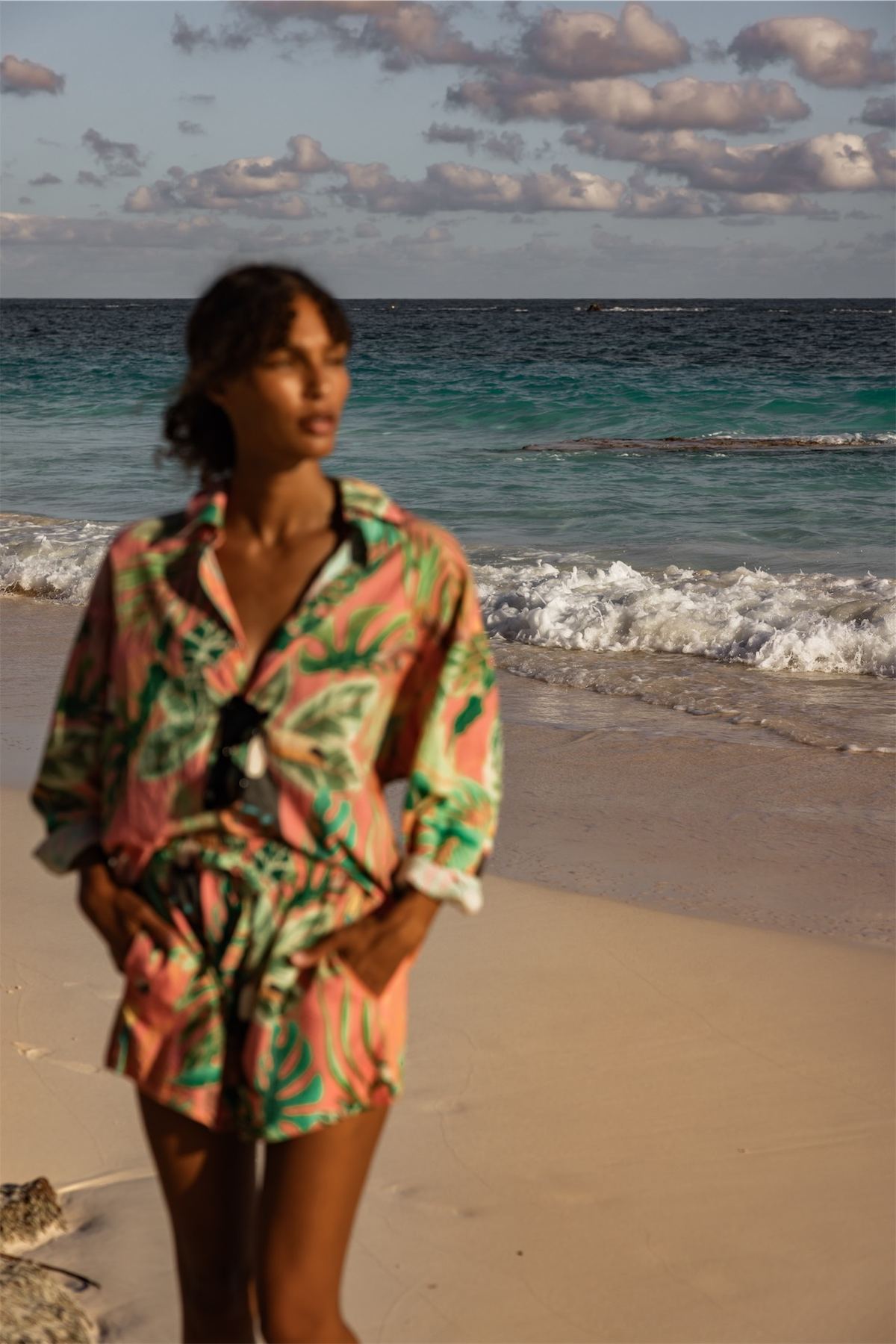 Model in a tropical print shirt and shorts walking the water's edge