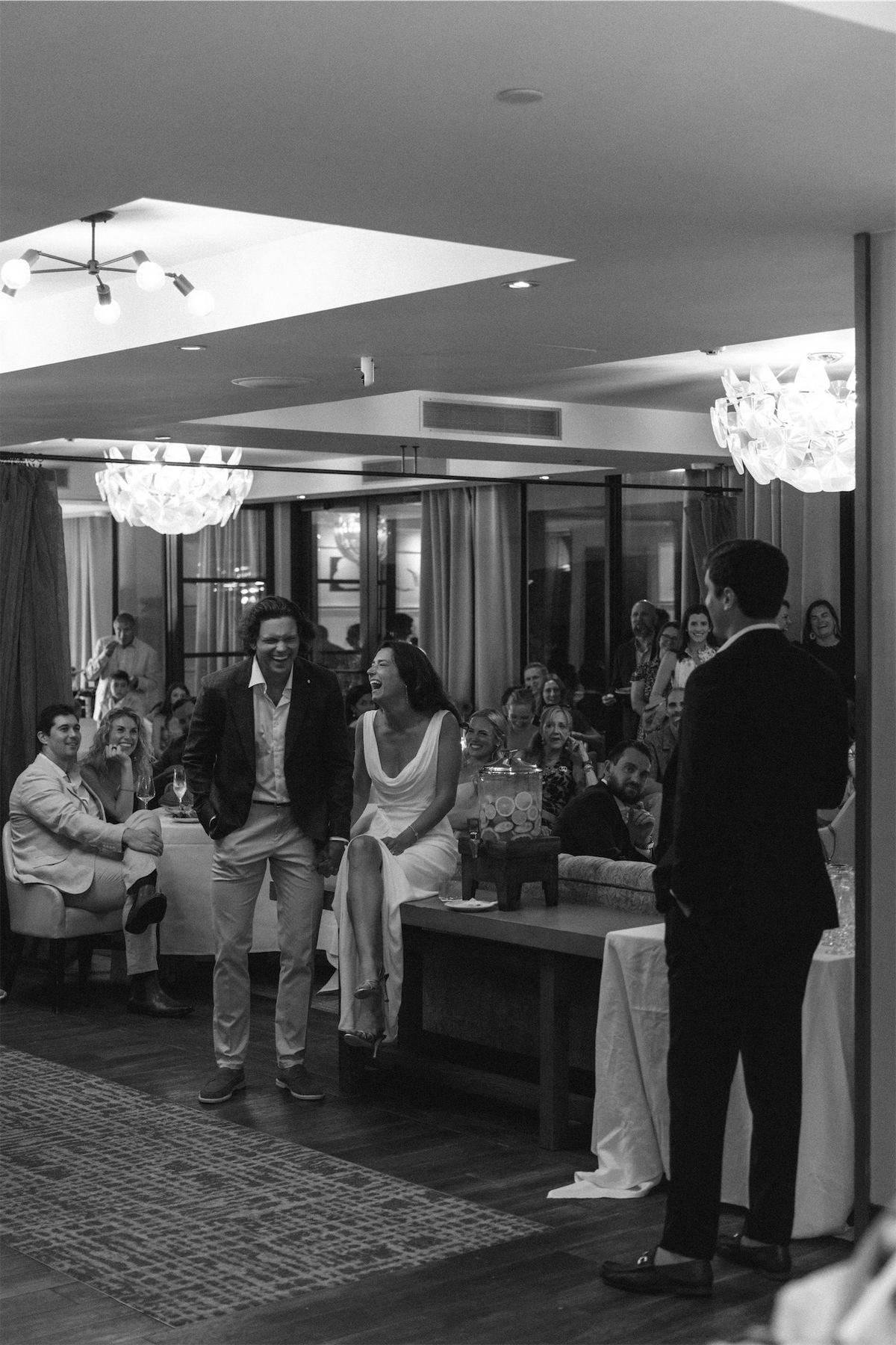 Black and white view of guests mingling at a welcome dinner in a bright dining room