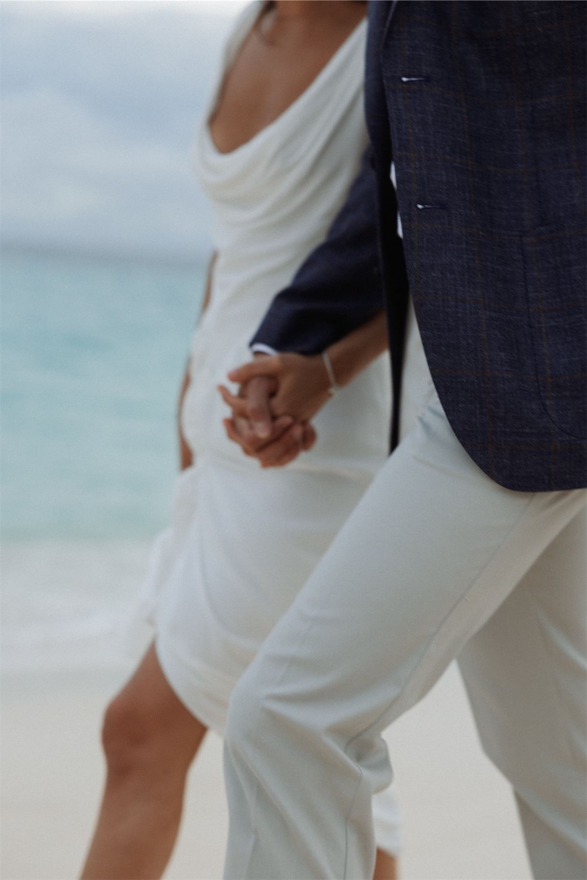 Cropped frame of the couple holding hands as they walk the shoreline in white