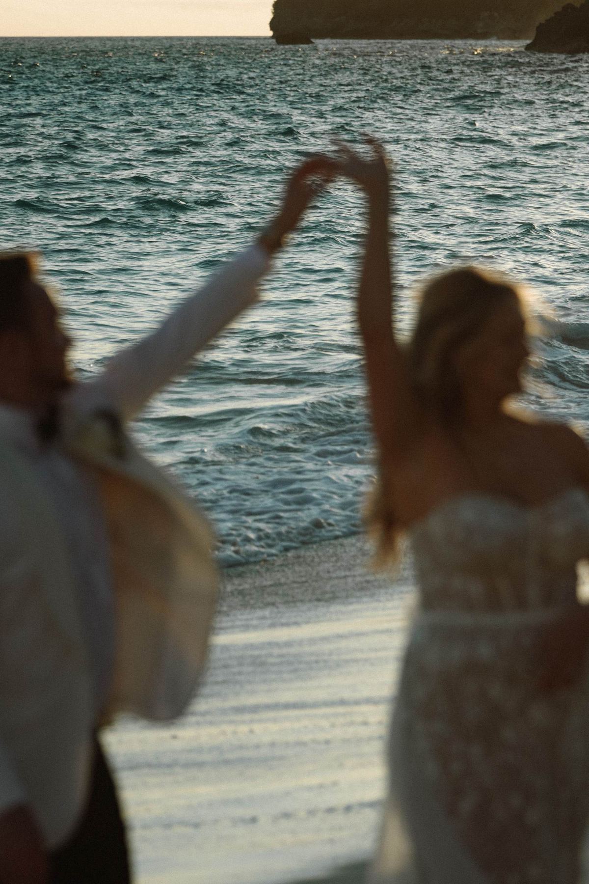 Bride and groom dancing arms raised at sunset on Bermuda beach