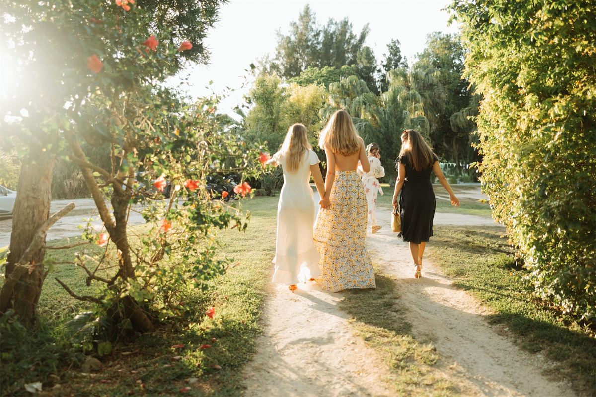 Bride walking a garden path with two women through low golden light and hibiscus