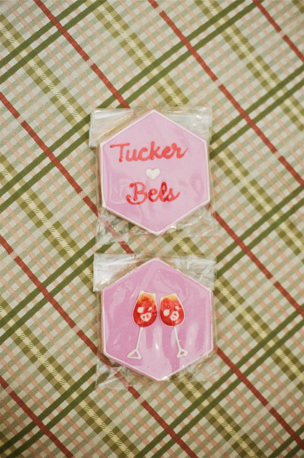 Pink iced wedding cookies naming the couple, arranged on a plaid cloth