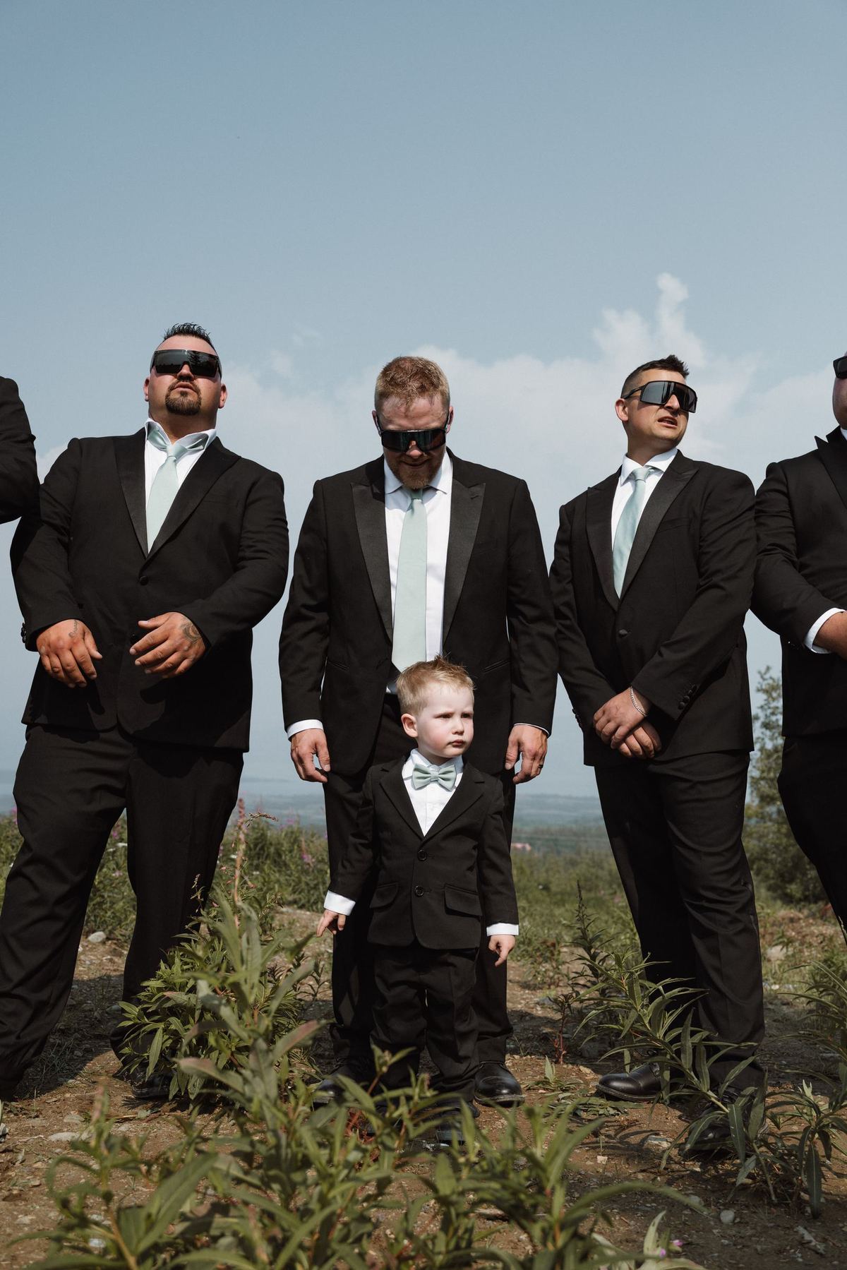 Groomsmen in black suits with the young ring bearer among them