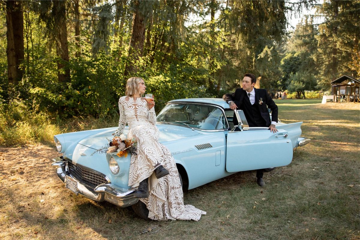 Bride and groom posing with a turquoise vintage convertible in the forest