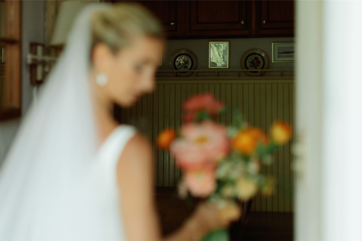 Bride in her veil carrying a bright bouquet through a doorway indoors