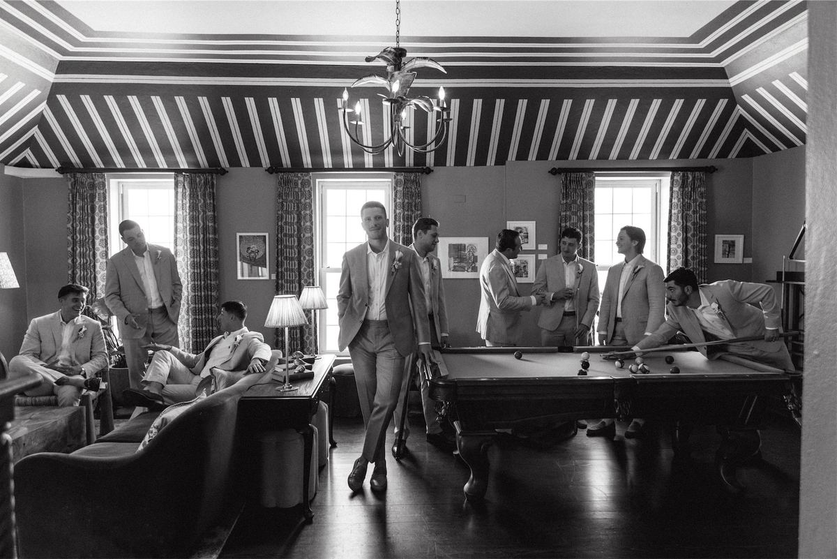 Black and white of the groomsmen around a pool table in a striped ceiling games room