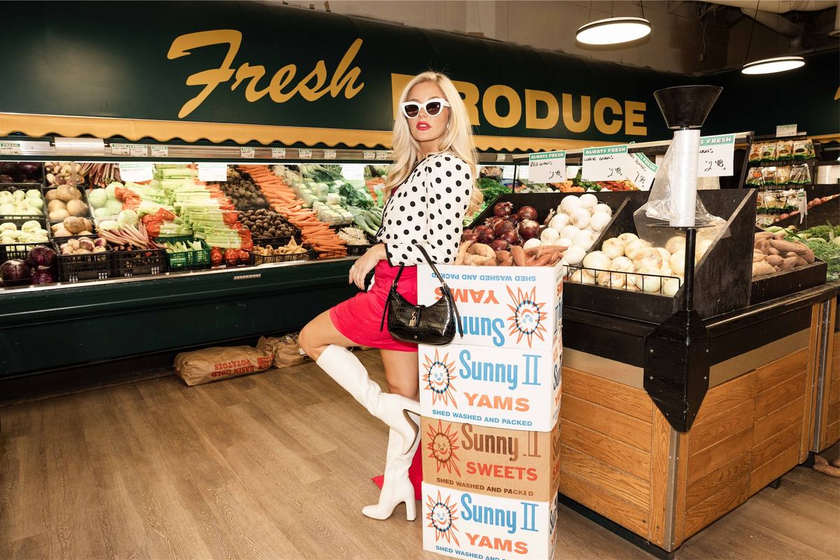 Model in polka dots and white boots perched on produce crates under a Fresh Produce sign