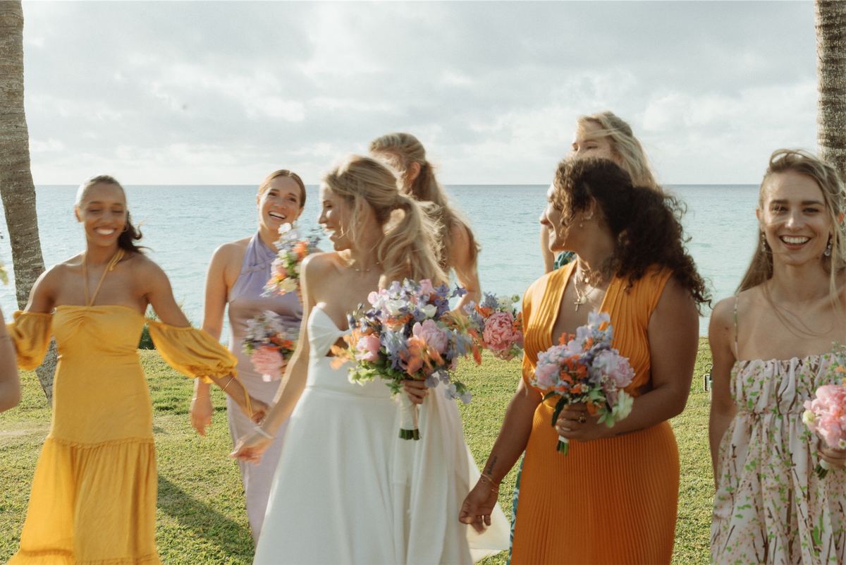 Bride walking the oceanfront lawn surrounded by bridesmaids in marigold dresses