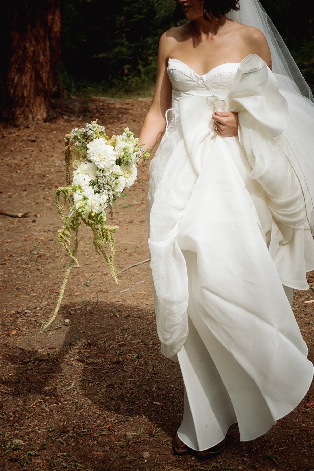 Devin lifts her gown walking the forest trail with her bouquet at a mountain ranch among the aspens