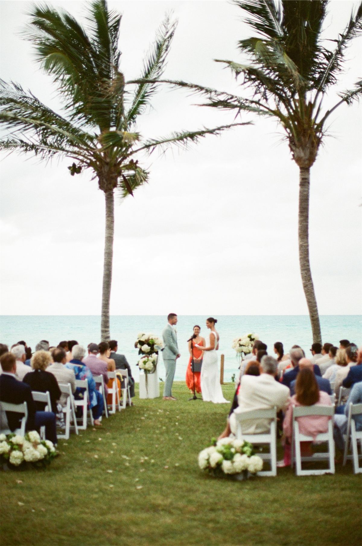 Guests seated for the ceremony on the lawn beneath tall palms by the water