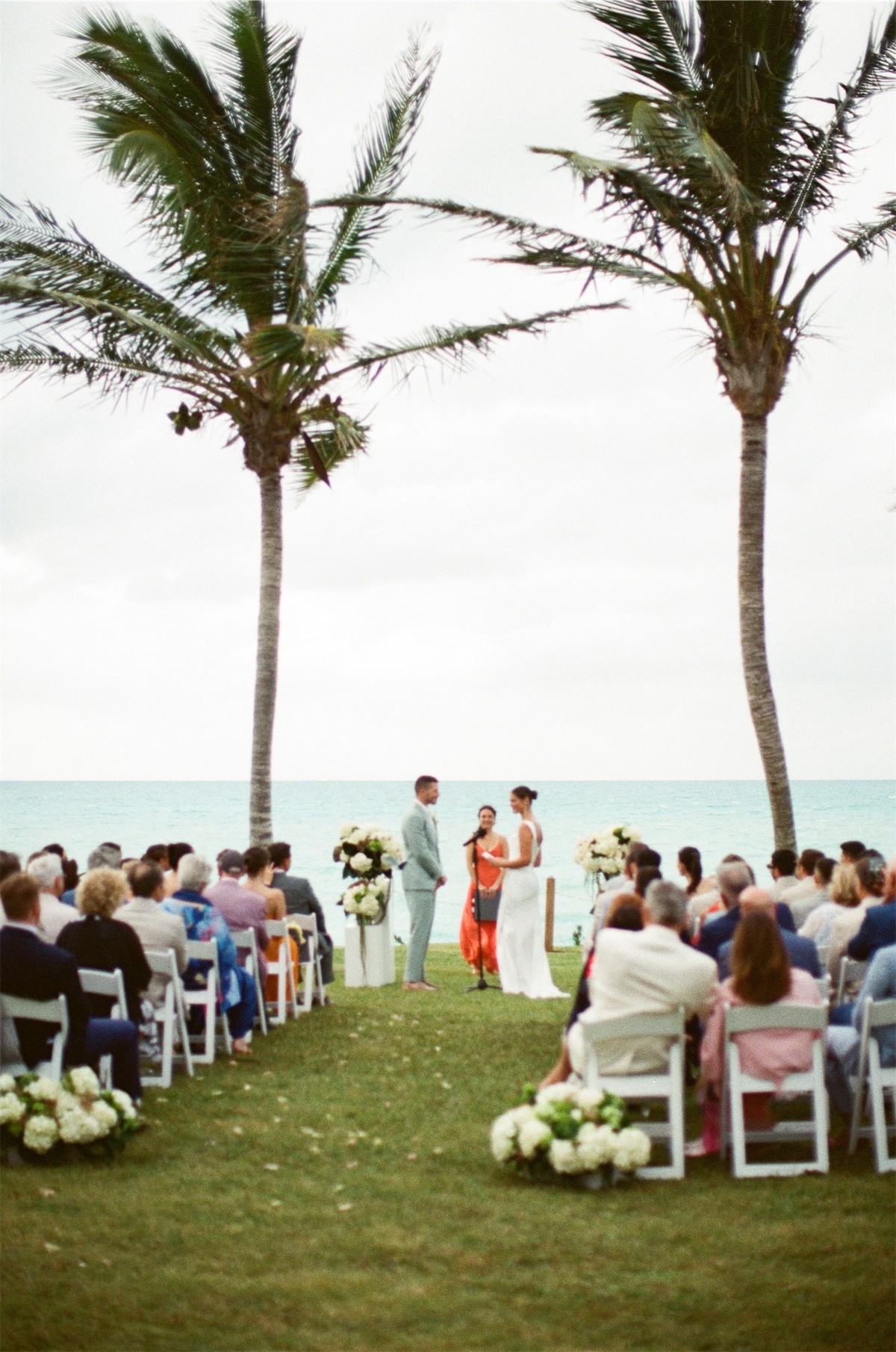 Guests seated for the ceremony on the lawn beneath tall palms by the water