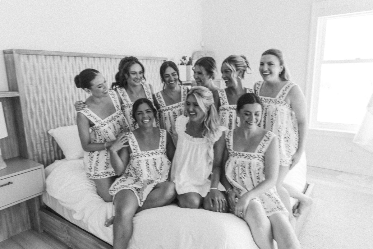 Bridesmaids in matching pajamas crowd around Paige on the bed on Hawkins Island, Bermuda, black and white