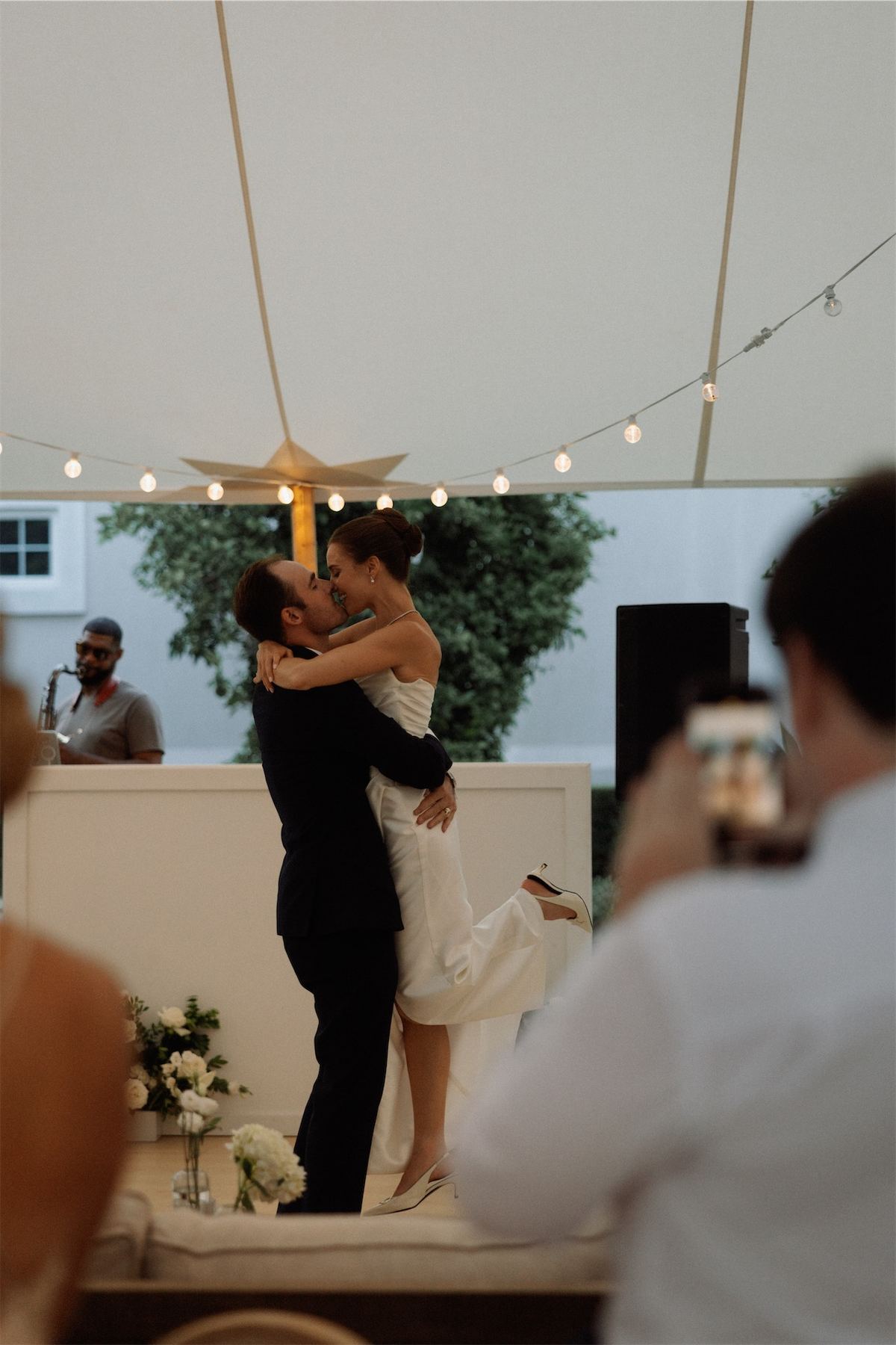 Couple dancing on a small stage while a guest films on a phone