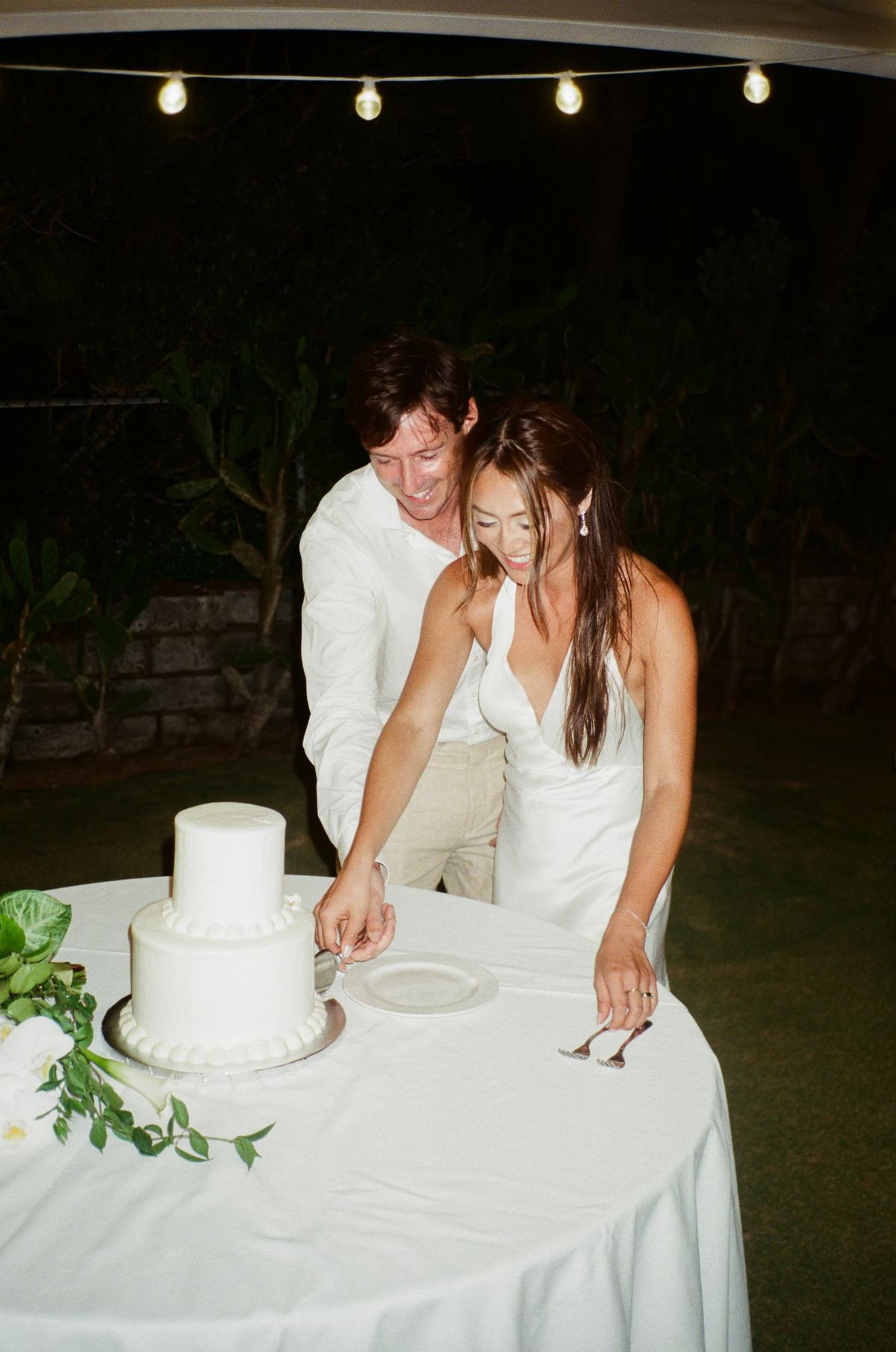 Bride and groom cutting their cake under string lights, shot on film