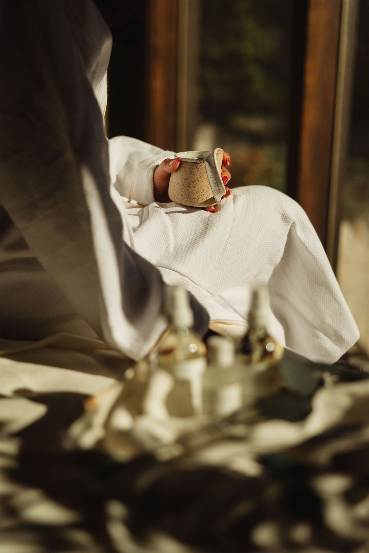 Hand reaching for a ceramic cup on the bed beside a tray of oils