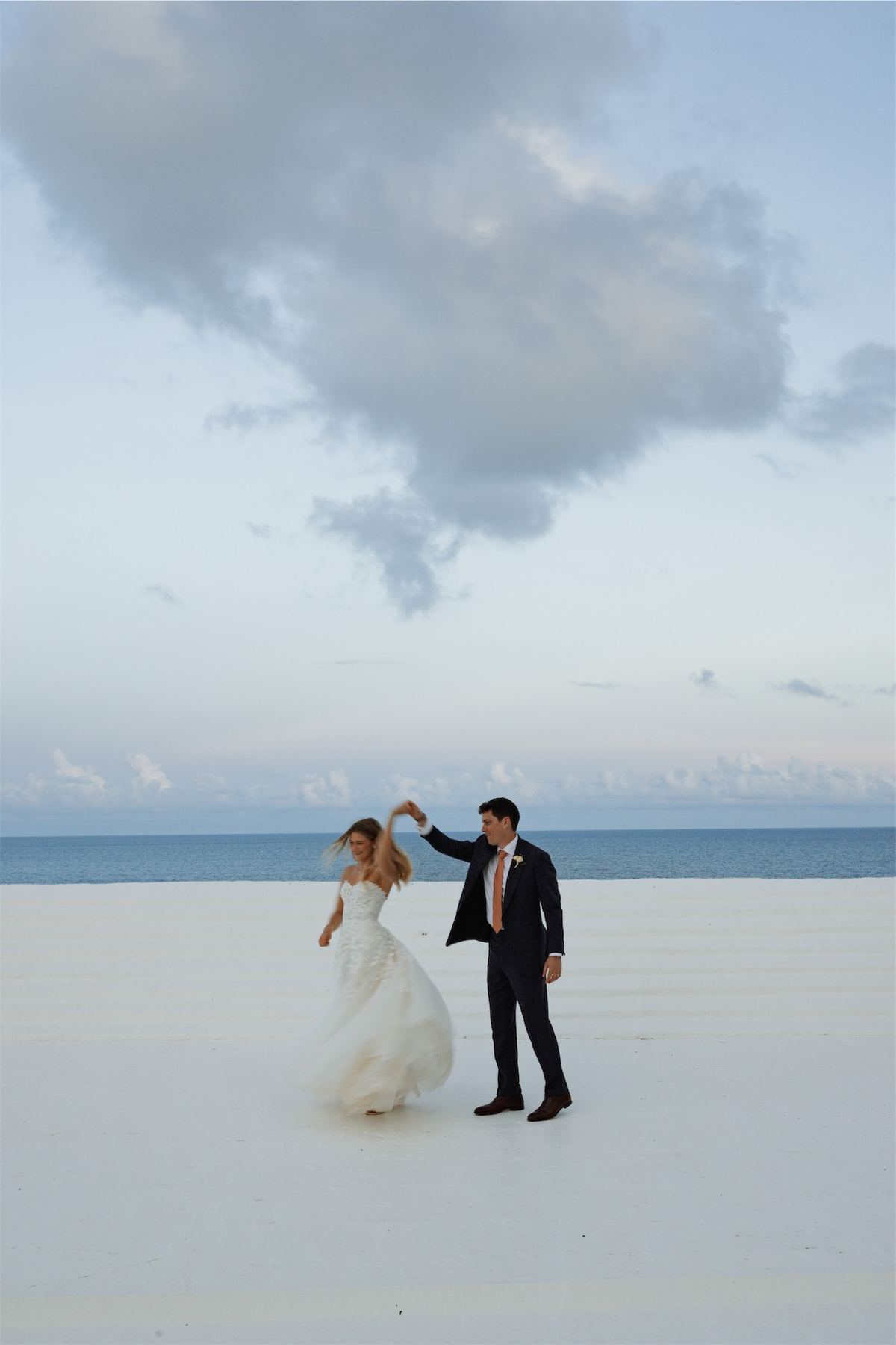 Groom twirling the bride on an empty stretch of pale sand beach